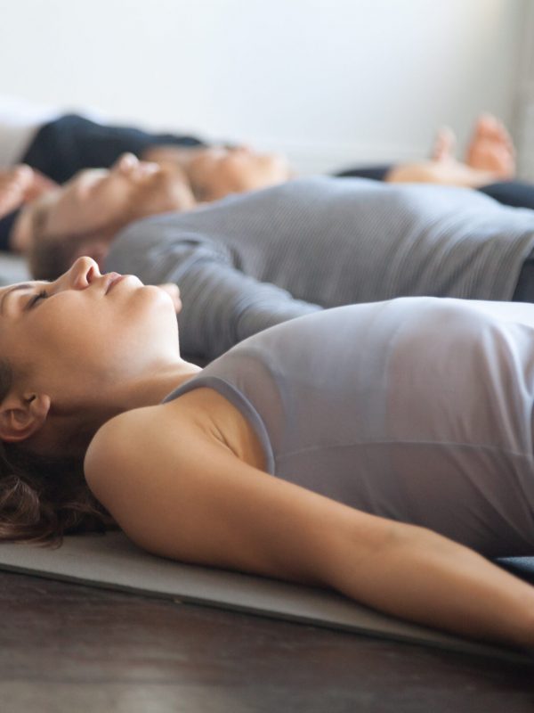Group of young sporty people practicing yoga lesson with instructor in gym, lying in Dead Body exercise, doing Savasana, Corpse pose, friends relaxing after working out in sport club, studio image